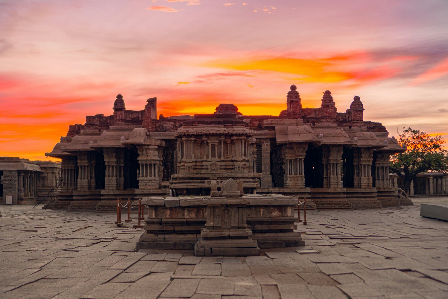 Stone pavilion and temple structures at Hampi under a vivid sunset sky